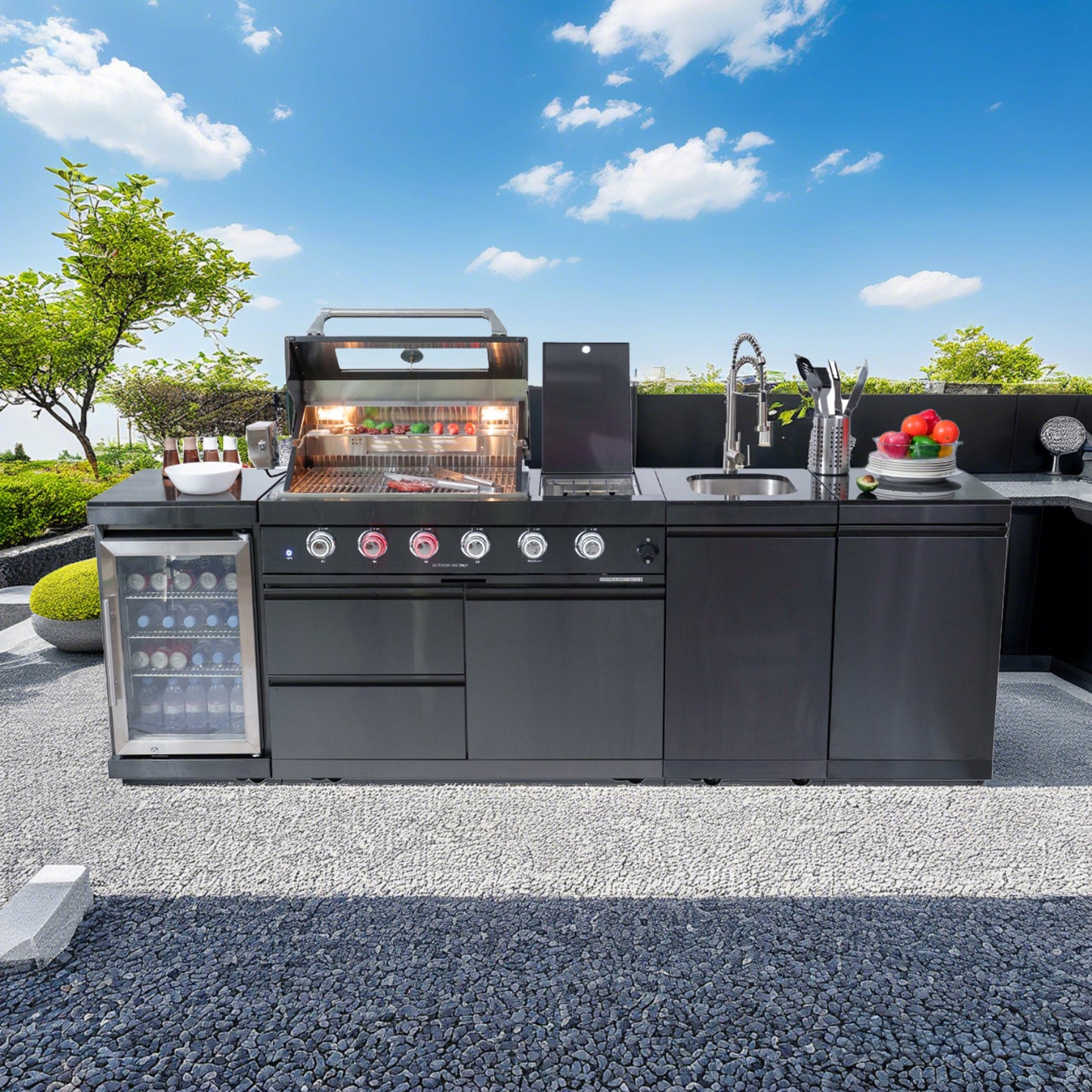 Outdoor kitchen with grill, refrigerator, and sink under a clear blue sky.