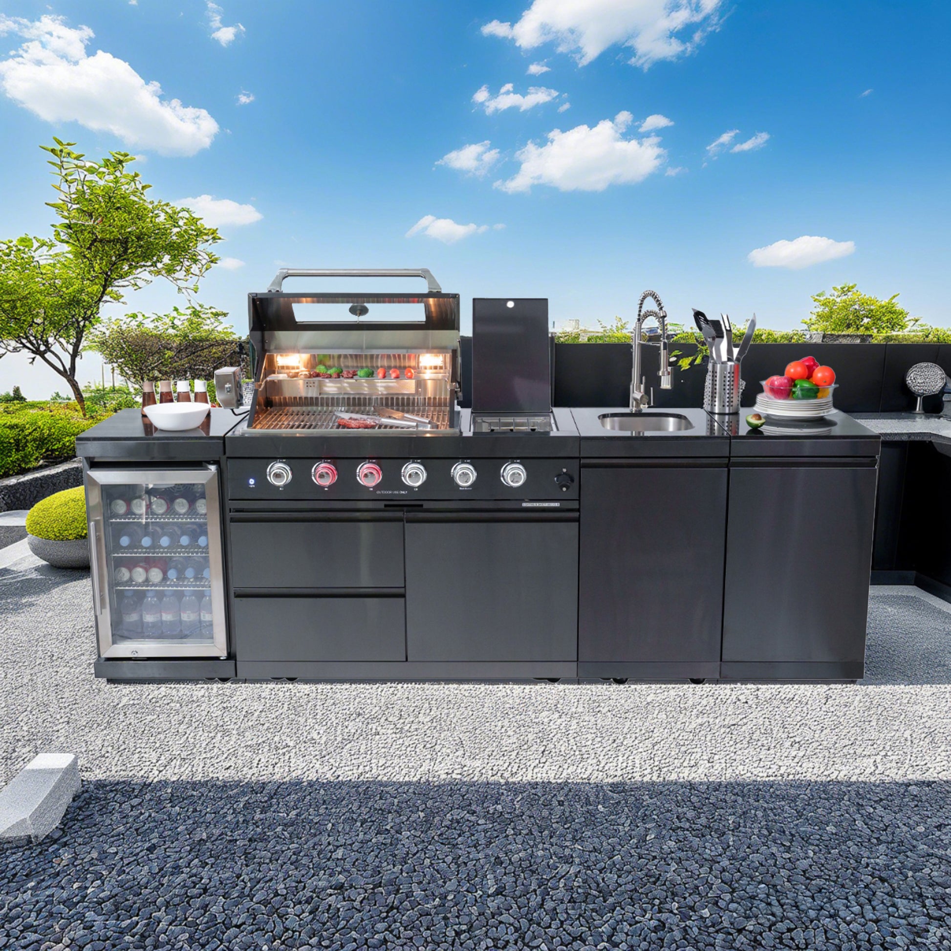 Outdoor kitchen with grill, refrigerator, and sink under a clear blue sky.