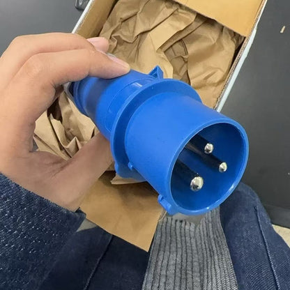 Hand holding a blue electrical plug with a cardboard box in the background