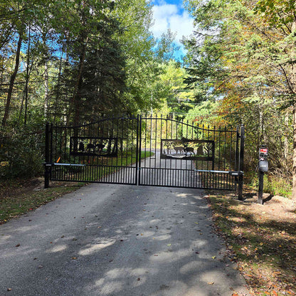 Black metal gate at the end of a driveway surrounded by trees