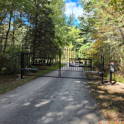 Black metal gate at the end of a driveway surrounded by trees
