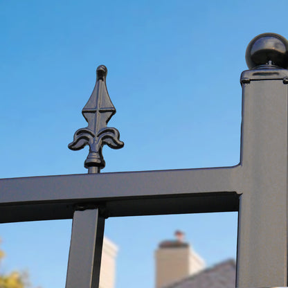 Close-up of a black metal fence or gate with a decorative fleur-de-lis finial and a post topped with a round ball
