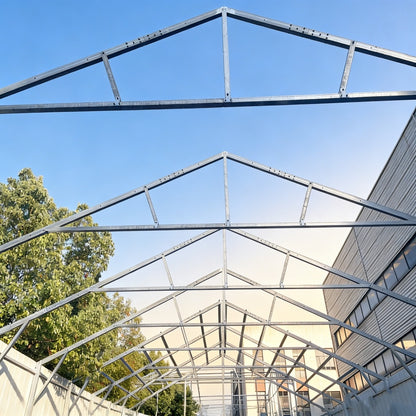 Metal frame structure against a blue sky with trees and a building in the background