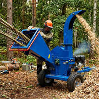 Person operating a blue wood chipper in a forest setting