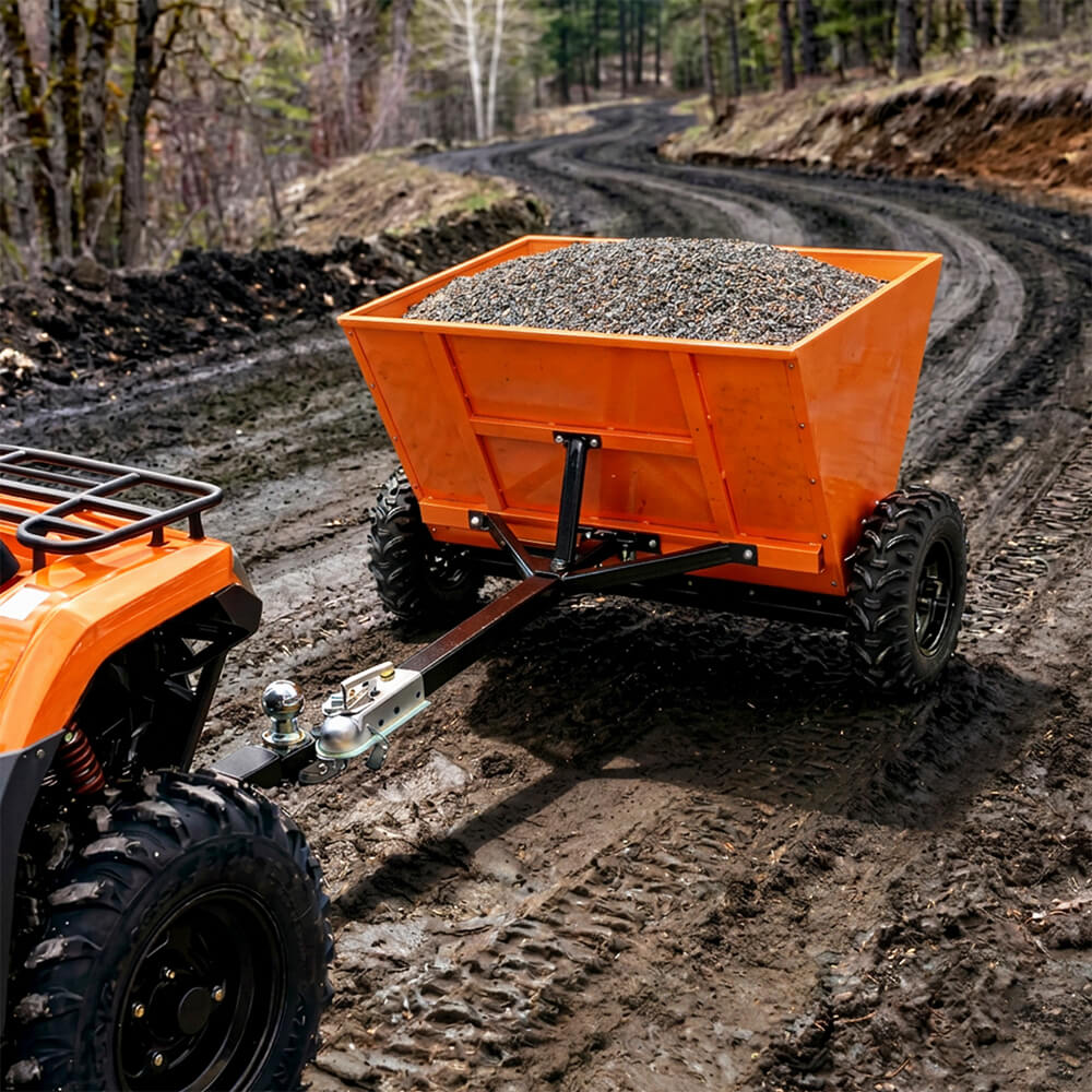 Orange dump trailer attached to a four-wheeler on a muddy trail with gravel load