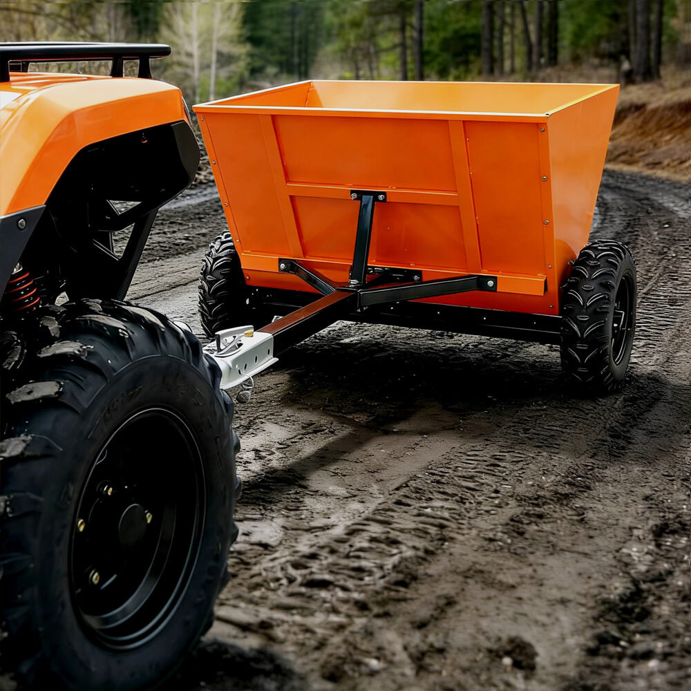 Orange dump trailer attached to a vehicle on a muddy road with trees in the background