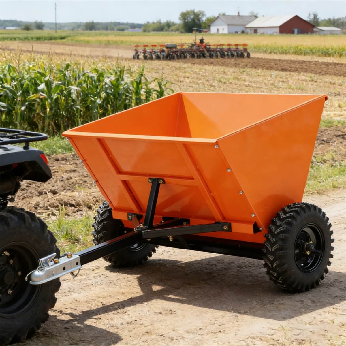 Orange dump trailer attached to an ATV in a field with farming equipment in the background.