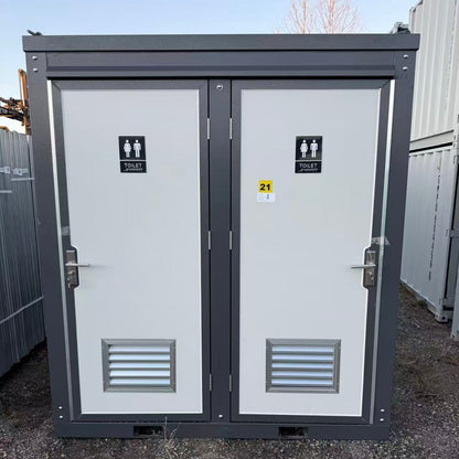 Portable toilet cabin with gender signs on doors, set against a clear sky.