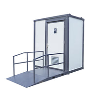 A portable restroom cabin with a gray metal frame, white door and walls, and a ramp with handrails