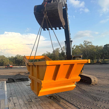 Large orange construction bucket attached to a crane with a clear sky and trees in the background.