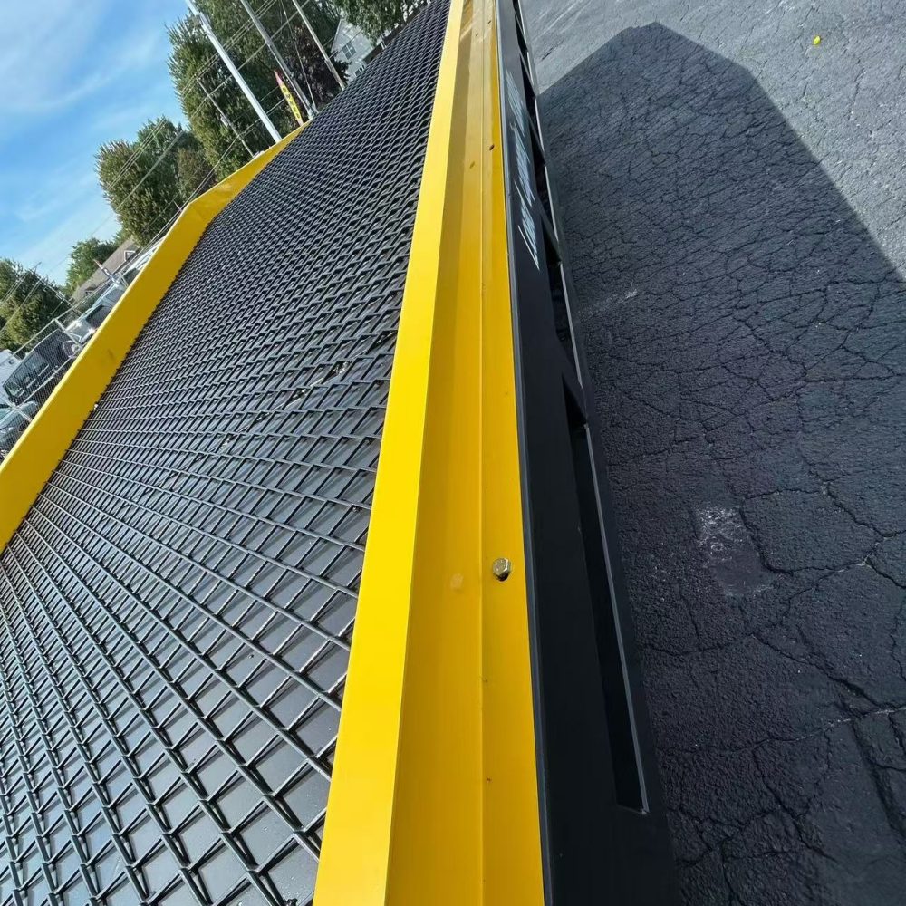 Yellow and black textured ramp on a paved surface with trees and vehicles in the background.
